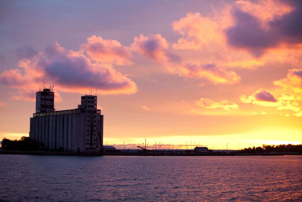 A painters in Collingwood create a masterpiece as they capture the breathtaking sight of a grain silo on a tranquil body of water during a picturesque sunset.