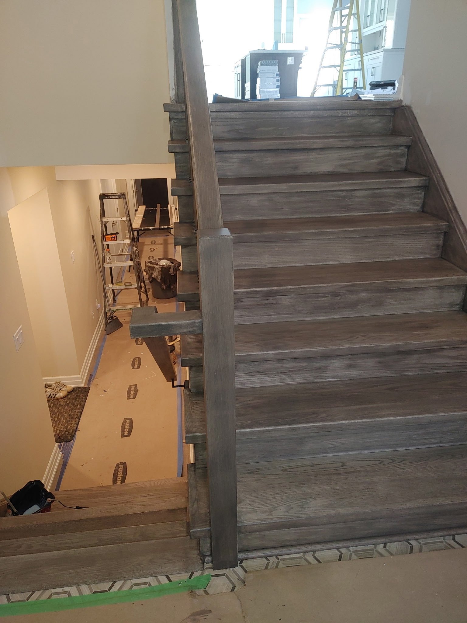 Wooden staircase under construction, with protective coverings and a ladder in the background.