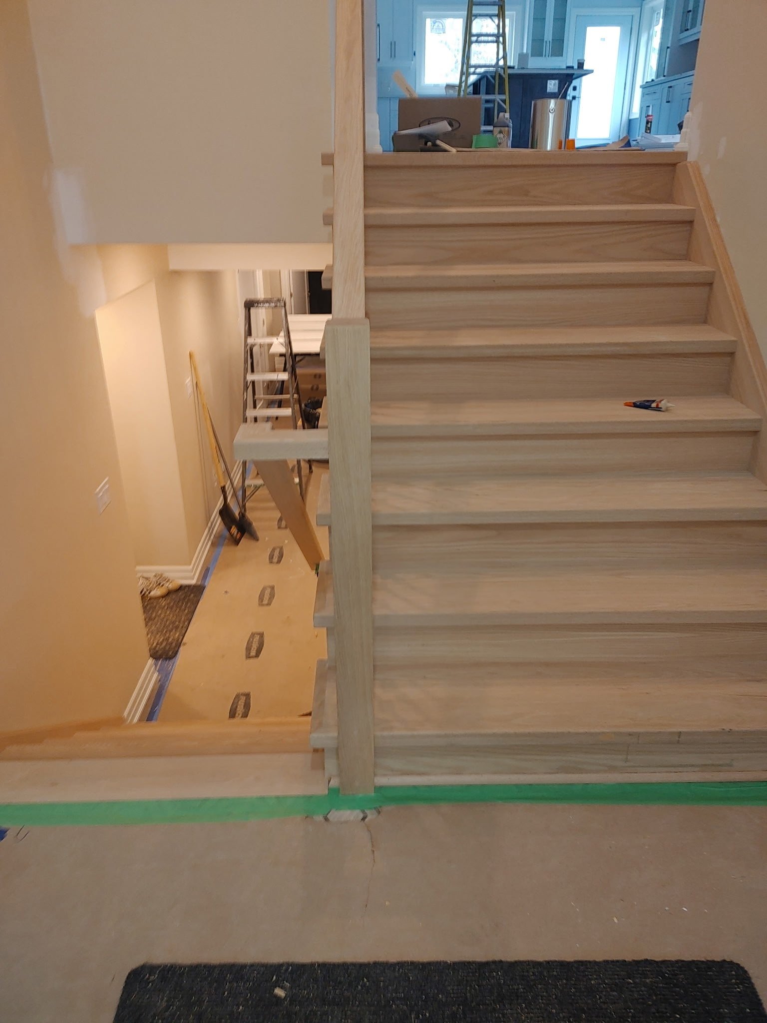 A set of unfinished wooden stairs with tools on the steps. A hallway and a room with ladders are visible in the background.