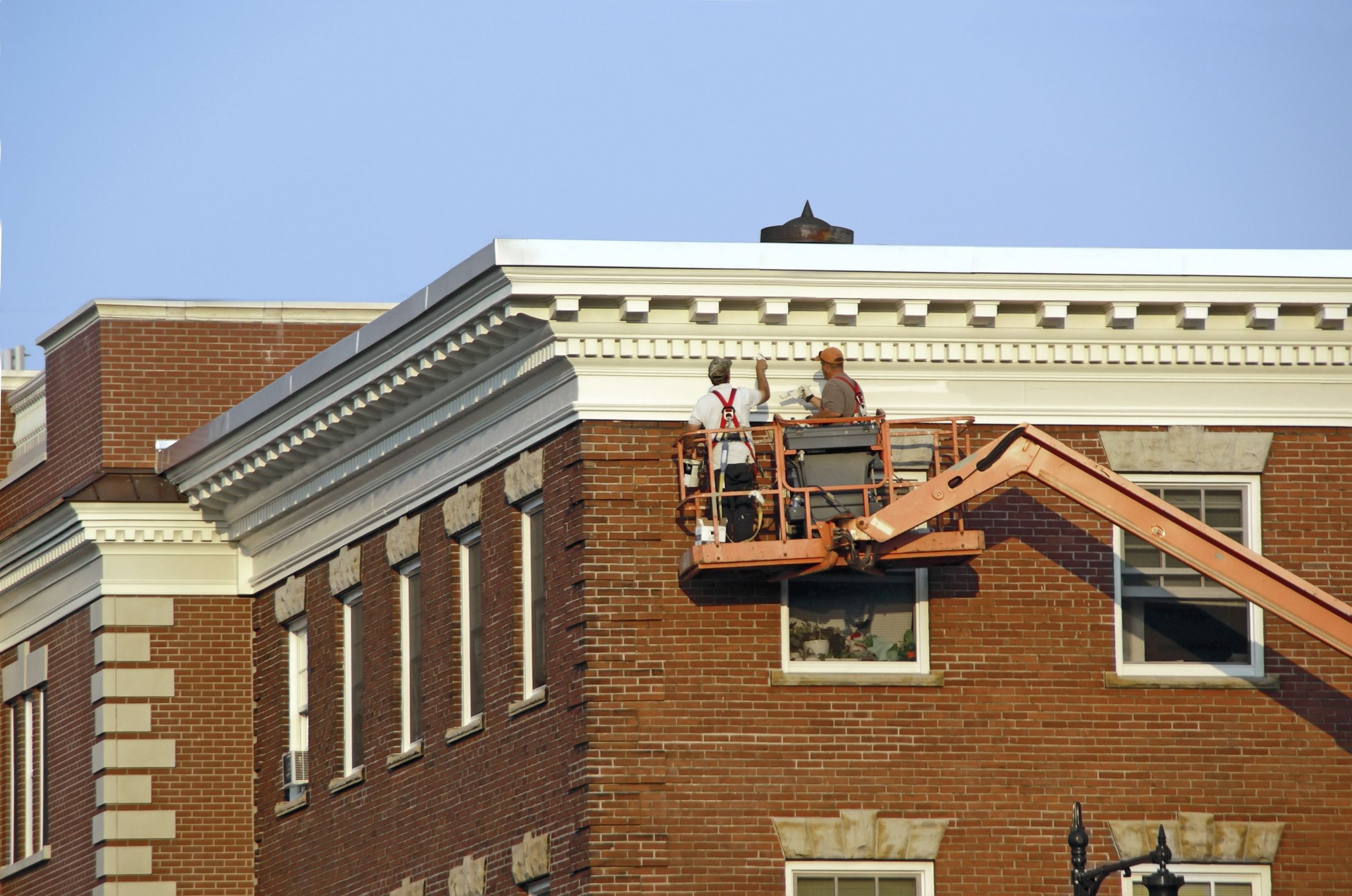Two workers on a lift inspecting the facade of a brick building.