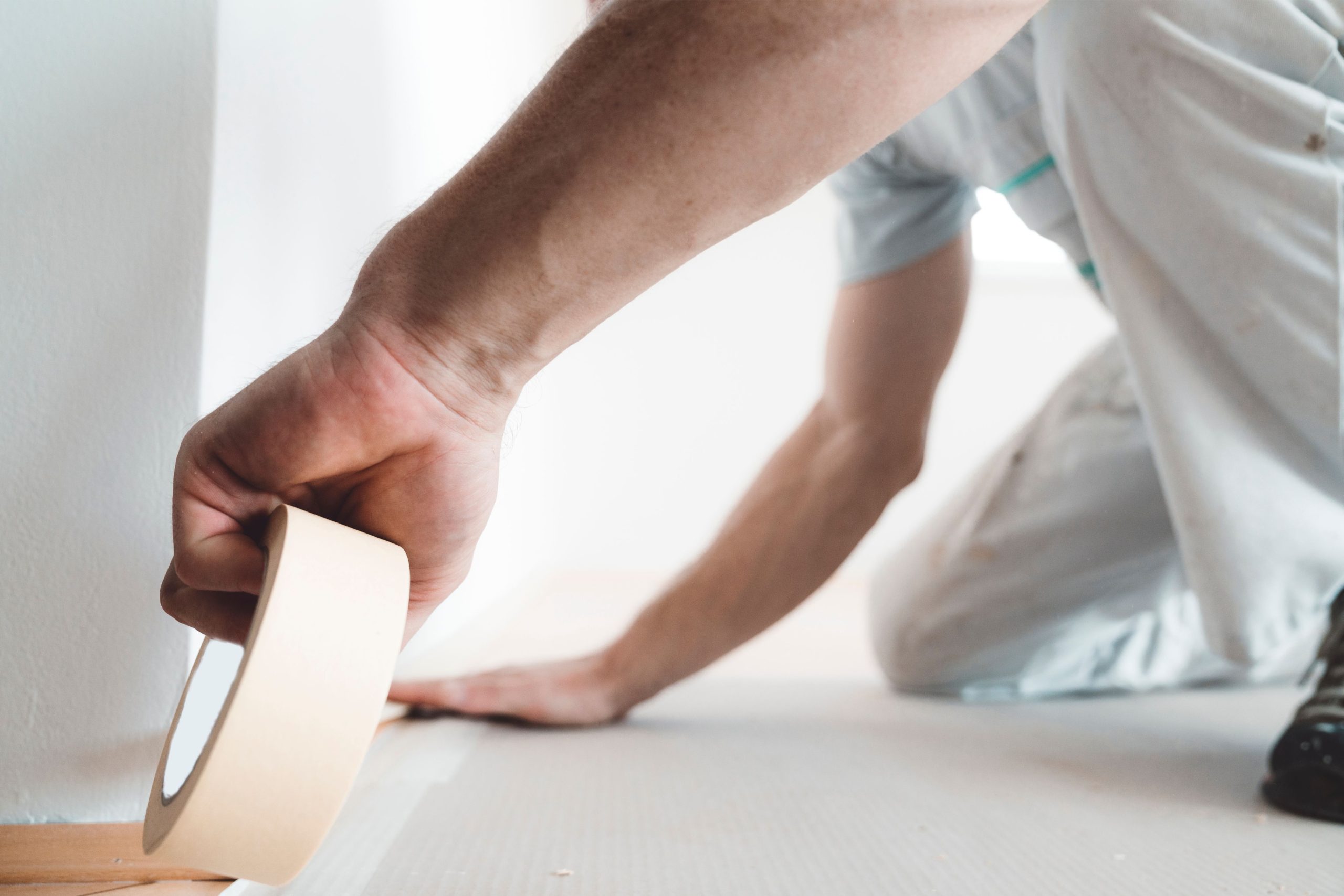 Person applying masking tape to the edge of a floor for painting preparation by reliable painters in Wasaga Beach.