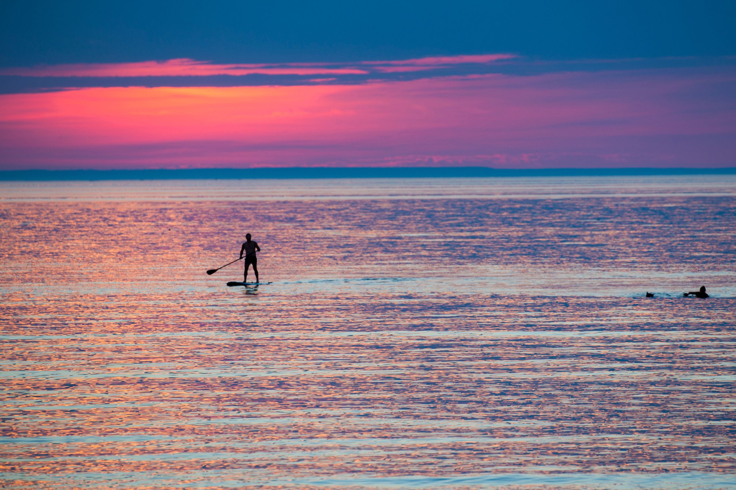Person paddleboarding on tranquil water at sunset near a scene of residential painting in Wasaga Beach.