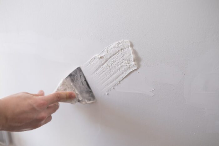 Applying spackle to a wall with a putty knife.