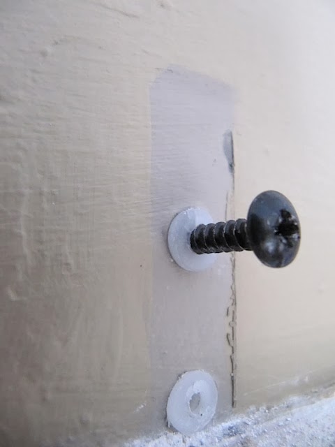 A close-up view of a black screw partially driven into a white surface with a small gap showing where the layers of material do not align perfectly.