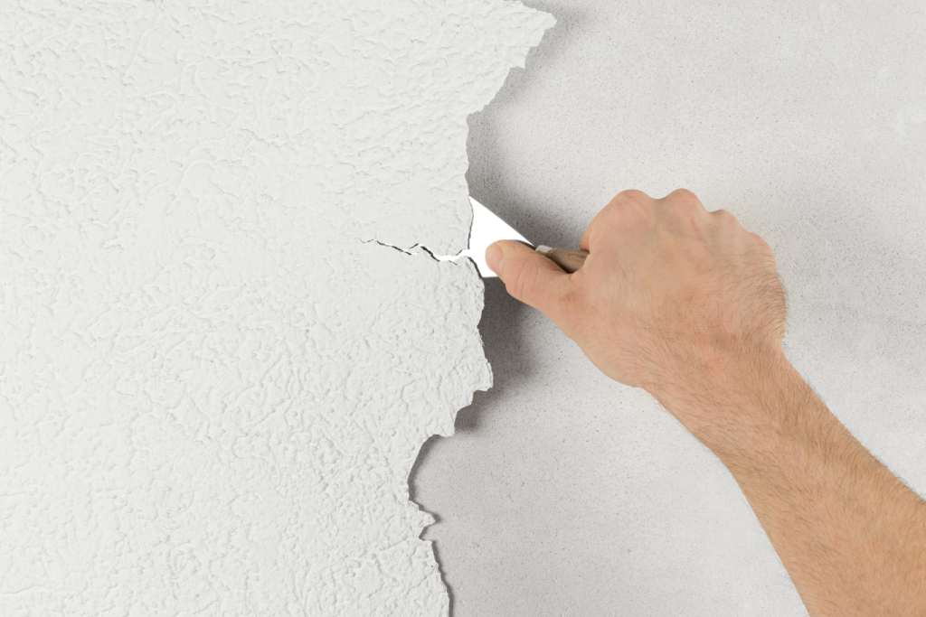 Scraping cracked paint off a wall using a putty knife.